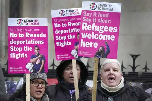 Stand Up To Racism campaigners hold banners outside the High Court in London, Monday, Dec. 19, 2022. Judges at Britain’s High Court say the U.K. government’s controversial plan to send asylum-seekers on a one-way trip to Rwanda is legal. But two judges also ruled that the government failed to consider the circumstances of the individuals it tried to deport. (AP Photo/Kirsty Wigglesworth)