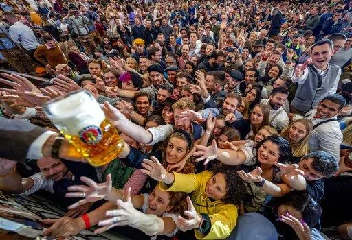 Young people reach out for free beer in one of the beer tents on the opening day of the 187th Oktoberfest beer festival in Munich, Germany, Saturday, Sept. 17, 2022. Oktoberfest is back in Germany after two years of pandemic cancellations, the same bicep-challenging beer mugs, fat-dripping pork knuckles, pretzels the size of dinner plates, men in leather shorts and women in cleavage-baring traditional dresses.  (AP Photo/Michael Probst)