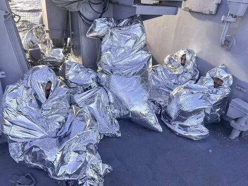 In this photo provided by the Greek Coast Guard, some of the nine men who survived a shipwreck and were found on an uninhabited islet are covered with a thermal blankets as they sit aboard a Greek Coast guard vessel, in the Aegean Sea, Greece, on Tuesday, Nov. 1, 2022. A major search and rescue operation was underway Tuesday for dozens of people missing after the boat they were on capsized and sank in stormy weather overnight off the coast of an island near the Greek capital. The coast guard sai