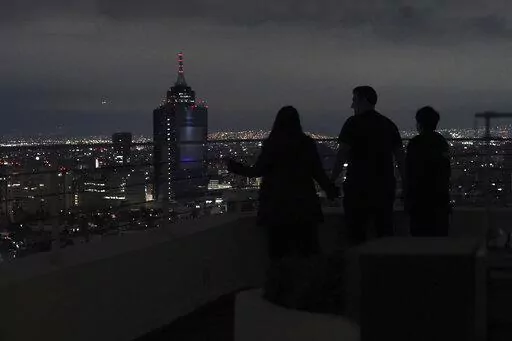 A family looks out at Mexico City from their apartment building rooftop after an earthquake early Thursday, Sept. 22, 2022. The magnitude 6.8 quake struck at 1:19 a.m. local time, causing at least two deaths, damaging buildings and setting off landslides near the epicenter in the western state of Michoacan. (AP Photo/Marco Ugarte)