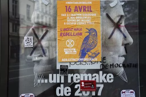 A torn front page ad shows incubent President Emmanuel Macron and challenger Marine Le Pen as the environmental group Extinction Rebellion takes part in a three-day demonstration against what they call France's inaction on climate issues, in the district of Porte de Saint Denis in the center of Paris, France, Monday, April 18, 2022. French President Emmanuel Macron is in pole position to win reelection Sunday, April 24, 2022 in France's presidential runoff. Yet his lead over far-right rival Mari