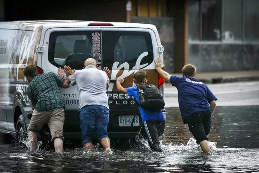 A stalled vehicle is pushed from flood waters following a rainstorm in Norfolk, Va., on Thursday, Aug. 6, 2020. The increasing threat of sea-level rise on Virginia’s coast means that an afternoon rainstorm can strand drivers for hours and damage cars beyond repair. The city of Norfolk is trying to do something about that. Officials have partnered with the tech firm FloodMapp and the Waze traffic app to warn residents of flooded roadways in real time. (Kristen Zeis/The Virginian-Pilot via AP)