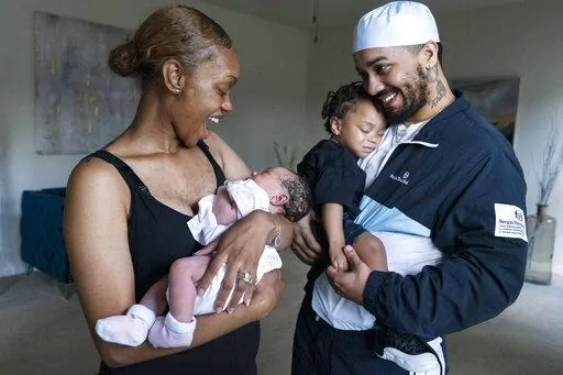 Aaliyah Wright, 25, of Washington, reacts on seeing a smile from her newborn daughter Kali, as her husband Kainan Wright, 24, of Washington, holds their son Khaza, 1, during a visit to the children's grandmother in Accokeek, Md., Tuesday, Aug. 9, 2022. A landmark social program is being pioneered in the nation’s capital. Coined “Baby Bonds,” the program is designed to narrow the wealth gap. The program would provide children of the city’s poorest families up to $25,000 when they reach ad