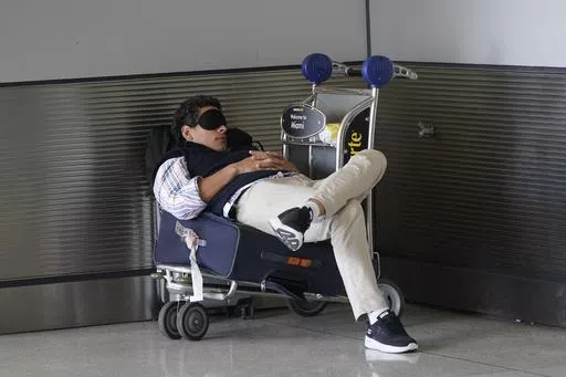 A traveler takes a nap as he waits for a ride outside Miami International Airport, Friday, July 1, 2022, in Miami. The Gallup survey, released Monday, April 15, 2024, says that a majority of Americans say they would feel better if they could have more sleep. But in the U.S., where the ethos of grinding and pulling yourself up by your own bootstraps is ubiquitous, getting enough sleep can seem like a dream. (AP Photo/Wilfredo Lee, File)