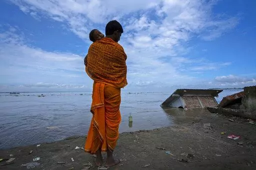 Ranajit Mandal, 35, the priest of a temple of Hindu goddess Durga stands with his son watching the temple being washed away by the river Brahmaputra at Murkata village, northeastern Assam state, India, Thursday, Oct. 13, 2022. "The river has washed away everything, and we have no place to go back to now," he said. "Even though we are staying nearby now, if this continues, we'll have no choice but to move away from here, away from the river." (AP Photo/Anupam Nath)
