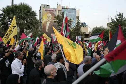 Iranian protesters wave Iranian, Palestinian and Lebanon's militant Hezbollah group flags in a demonstration to condemn the killing of Hamas leader Ismail Haniyeh as a huge portrait of him is seen on a wall at background, at Felestin (Palestine) Sq. in Tehran, Iran, Wednesday, July 31, 2024. Two back-to-back strikes in Beirut and Tehran, both attributed to Israel and targeting high-ranking figures in Hezbollah and Hamas, have left Hezbollah and Iran in a quandary. (AP Photo/Vahid Salemi)