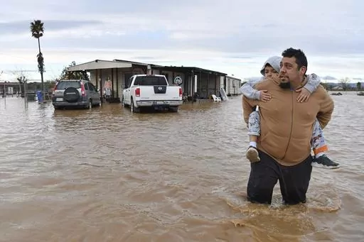 Ryan Orosco, of Brentwood, carries his son Johnny, 7, on his back while his wife Amanda Orosco waits at the front porch to be rescued from their flooded home on Bixler Road in Brentwood, Calif., Jan. 16, 2023. The National Oceanic and Atmospheric Administration announced Monday, Sept. 11, that there have been 23 weather extreme events in America that cost at least $1 billion this year through August, eclipsing the year-long record total of 22 set in 2020. (Jose Carlos Fajardo/Bay Area News Group