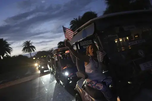 A supporter of Democratic presidential nominee Vice President Kamala Harris waves an American flag and cheers as she participates in a golf cart parade following a campaign event with second gentleman Doug Emhoff, in The Villages, Fla., Friday, Sept. 13, 2024. (AP Photo/Rebecca Blackwell)