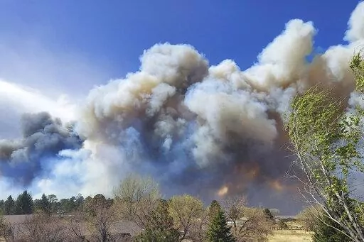 Smoke from a wind-whipped wildfire rises above neighborhoods on the outskirts of Flagstaff, Ariz., on Tuesday, April 19, 2022. Homes on the outskirts of Flagstaff were being evacuated Tuesday as high winds whipped a wildfire, shut down a major highway and grounded firefighting aircraft. (Sean Golightly/Arizona Daily Sun via AP)