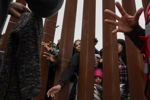 Migrants reach through a border wall for clothing handed out by volunteers as they wait between two border walls to apply for asylum Friday, May 12, 2023, in San Diego. Hundreds of migrants remain waiting between the two walls, many for days. The image was part of a series by Associated Press photographers Ivan Valencia, Eduardo Verdugo, Felix Marquez, Marco Ugarte Fernando Llano, Eric Gay, Gregory Bull and Christian Chavez that won the 2024 Pulitzer Prize for feature photography. (AP Photo/Greg