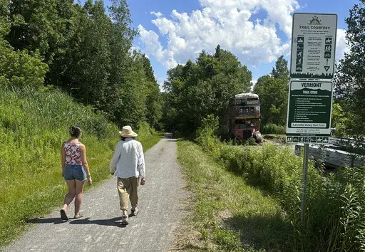 Two people walk on the Lamoille Valley Rail Trail in Jeffersonville, Vt., on Friday July 5, 2024. The 93-mile trail, which is open in the summer to all non-motorized users, is the longest rail trail in New England. (AP Photo/Wilson Ring)