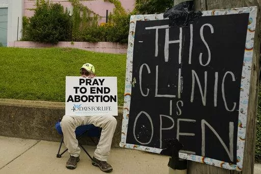 An anti-abortion supporter sits behind a sign that advises the Jackson Women's Health Organization clinic is still open in Jackson, Miss., Wednesday, July 6, 2022. (AP Photo/Rogelio V. Solis, File)