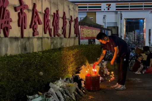 A man lights a candle near flowers placed outside the "Zhuhai People's Fitness Plaza", where a man deliberately rammed his car into people exercising at the sports center, killing some and injuring others in Zhuhai in southern China's Guangdong province, Nov. 12, 2024. (AP Photo/Ng Han Guan, File)