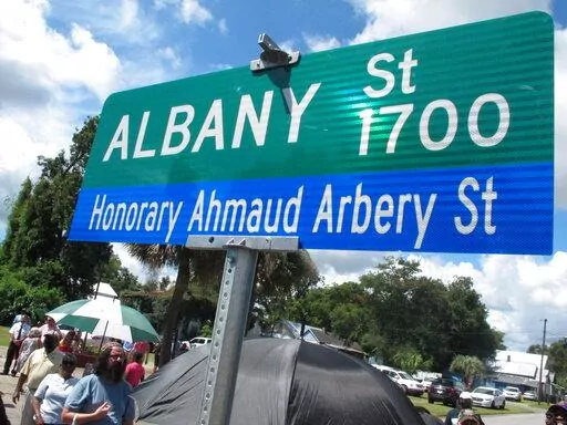 A crowd gathers under a new sign designating a city roadway as Honorary Ahmaud Arbery Street on Tuesday, Aug. 9, 2022, in Brunswick, Ga. City officials approved the honor for Arbery, a 25-year-old Black man who was fatally shot in February 2020 after being chased by three white men in pickup trucks who spotted him running in their neighborhood. All three men were later convicted of murder and federal hate crimes. (AP Photo/Russ Bynum)