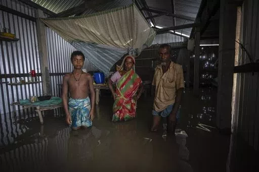 Yaad Ali, right, and his wife Monuwara Begum, center, and Musikur Alam, stand in their submerged house in Sandahkhaiti, a floating island village in the Brahmaputra River in Morigaon district, Assam, India, Wednesday, Aug. 30, 2023. The family move away with every flood, and move back to their house every dry season. (AP Photo/Anupam Nath, File)