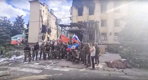 This photo taken from video provided by Ramzan Kadyrov's Official Telegram channel released on Saturday, July 2, 2022, shows Russian troops including soldiers of Chechen regiment waving Russian and Chechen republic national flags as they pose for a photo in front of a destroyed building in Lysychansk, Ukraine. After more than four months of ferocious fighting, Russia claimed full control over one of the two provinces in Ukraine’s eastern industrial heartland. (Ramzan Kadyrov's Official Telegra
