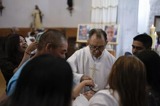 Rev. Jesus Reyes baptizes a child in the atrium of the Saint Francis Xavier Parish church in Cerocahui, Mexico, Sunday, May 12, 2024. In this area of the church, Reyes witnessed the shooting of two of his fellow Jesuit priests, Javier Campos and Joaquin Mora, when gang leader "El Chueco" shot them to death. (AP Photo/Eduardo Verdugo)