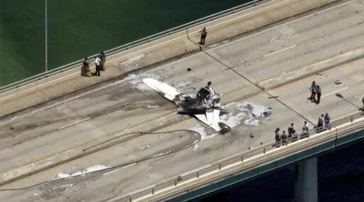 This photo provided by WSVN-TV emergency personnel respond to a small plane crash in Miami on Saturday, May 14, 2022. The small plane has crashed on a bridge near Miami, striking an SUV and bursting into flames. The Federal Aviation Administration reported the single-engine Cessna 172 lost power just before Saturday's crash. (WSVN-TV via AP)