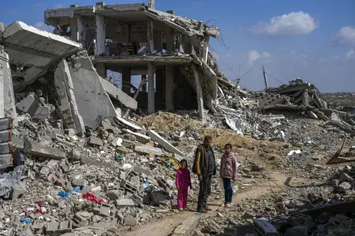 A Palestinian man and two girls stand a mid of the rubble of homes, destroyed by the Israeli army's air and ground offensive against Hamas in in Bureij refugee camp, central Gaza Strip, Monday, Feb. 17, 2025. (AP Photo/Abdel Kareem Hana)