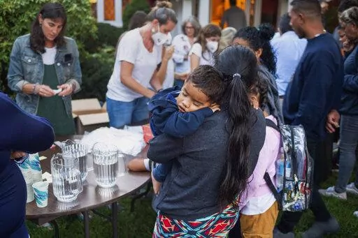 A woman, who is part of a group of immigrants that had just arrived, holds a child as they are fed outside St. Andrews Episcopal Church, Wednesday Sept. 14, 2022, in Edgartown, Mass., on Martha's Vineyard. Florida Gov. Ron DeSantis on Wednesday flew two planes of immigrants to Martha's Vineyard, escalating a tactic by Republican governors to draw attention to what they consider to be the Biden administration's failed border policies. (Ray Ewing/Vineyard Gazette via AP)