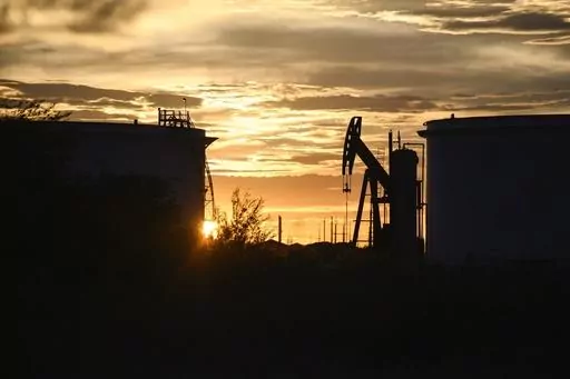 The sun begins to set behind crude oil tanks and a pumpjack, July 5, 2022, in Midland, Texas. The IEA’s annual world energy outlook, which analyzes the global picture of energy supply and demand, was released Tuesday, Oct. 24, 2023. (Eli Hartman/Odessa American via AP, File)