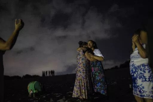 Mag Oliveira embraces her daughter Najla as they pray in an area of the Abaete dune system, on a steep rise of sand evangelicals have come to call the "Holy Mountain", in Salvador, Brazil, late Friday night, Sept. 16, 2022. Evangelicals have been converging on the dunes for some 25 years but especially lately, with thousands now coming each week to sing, pray and enter trancelike states to commune with God.(AP Photo/Rodrigo Abd)