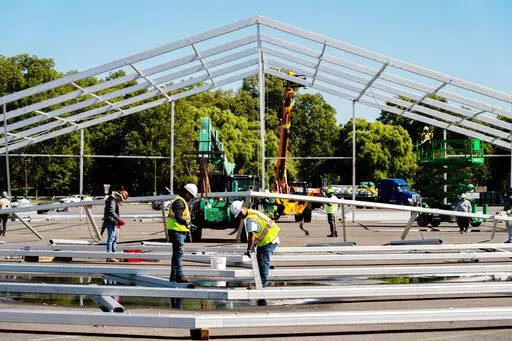 FILE — Workers erect a hangar-sized tent, Sept. 27, 2022, in the parking lot of Orchard Beach, in the Bronx borough of New York, as temporary shelter for thousands of international migrants who have been bused into the Big Apple. New York City's mayor Eric Adams declared a state of emergency on Friday, Oct. 7, over the thousands of migrants being sent from southern border states since the spring, saying the demand being put on the city to provide housing and other assistance is "not sustainabl