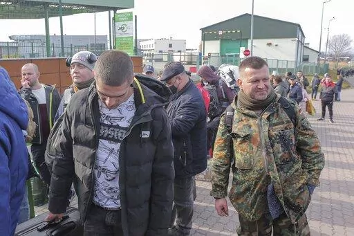 Polish volunteer Jedrzej, 34, in military uniform joins Ukranians, left, waiting to cross the border to go and fight against Russian forces, at Medyka border crossing, in Poland, Saturday, Feb. 26, 2022. (AP Photo/Visar Kryeziu)