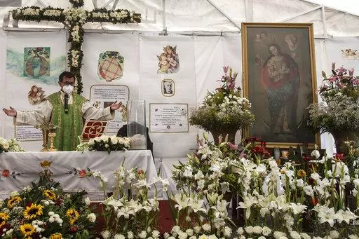 Rev. Adrian Vazquez celebrates an outdoor Mass under a white tent outside the quake-damaged Our Lady of the Angels church, in the working-class Guerrero neighborhood of Mexico City, Sunday, Aug. 7, 2022. Pictured right is a wax painting of Our Lady of the Angels, a replica of the one on the wall inside the church, home to the revered image of the Virgin Mary, its history dating to the end of the 16th century. (AP Photo/Ginnette Riquelme)