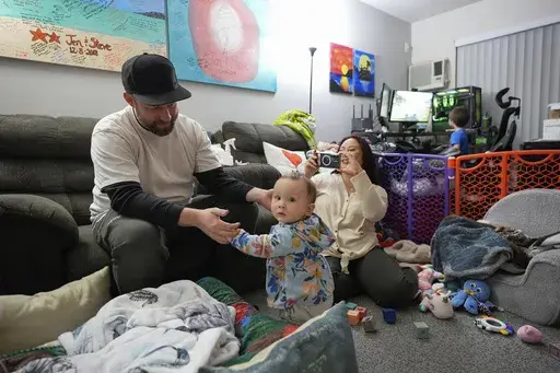 Steve Petersen, left, and his wife Jennifer watch as their daughter Carolynn tries to stand inside their apartment in Campbell, Calif., Wednesday, Jan. 15, 2025. (AP Photo/Godofredo A. Vásquez)