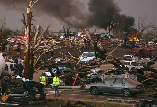 FILE- In this May 22, 2011 file photo, emergency personnel walk through a severely damaged neighborhood after a tornado hit Joplin, Mo. (AP Photo/Mark Schiefelbein, File)