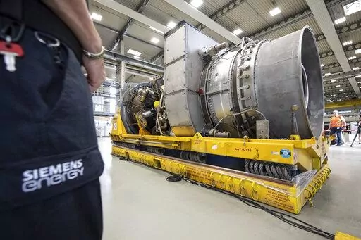 Employees stand around the turbine serviced in Canada for the Nordstream 1 natural gas pipeline in Muelheim an der Ruhr, Germany, Aug. 3, 2022. German Chancellor Olaf Scholz visited a plant by Siemens Energy where a turbine, which is at the center of a dispute between Germany and Russia over reduced gas supplies, is currently sitting in storage until it can be shipped to Russia. (Bernd Thissen/dpa via AP)