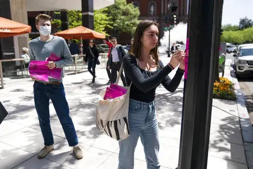 George Washington University student Kai Nilsen, left, watches as American University student Magnolia Mead as they put up posters near the White House promoting student loan debt forgiveness, Friday, April 29, 2022, in Washington. (AP Photo/Evan Vucci)