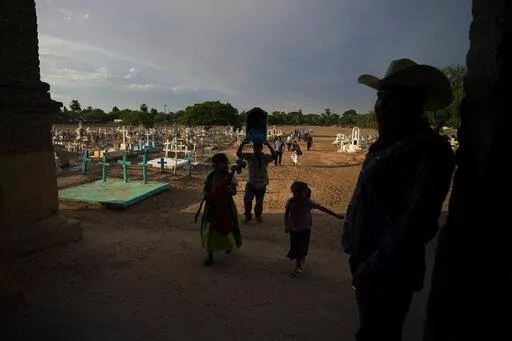A Yaqui Indigenous family walks past the cemetery where slain water-defense leader Tomás Rojo is buried, outside a church where they arrive to celebrate the Virgin Mary in Potam, Mexico, Tuesday, Sept. 27, 2022. Mexico has become the deadliest place in the world for environmental and land defense activists, and the Yaqui Indigenous people of northern Mexico are still mourning the killing of  Rojo in June 2021. (AP Photo/Fernando Llano)