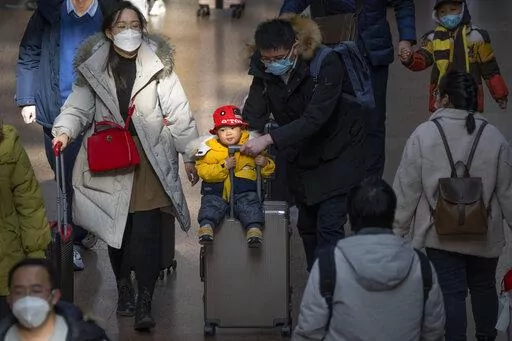 A man pushes a child riding on a suitcase at Beijing West Railway Station in Beijing, Wednesday, Jan. 18, 2023. A population that has crested and is slowly shrinking will pose new challenges for China's leaders, ranging from encouraging young people to start families, to persuading seniors to stay in the workforce longer and parents to allow their children to join the military. (AP Photo/Mark Schiefelbein)