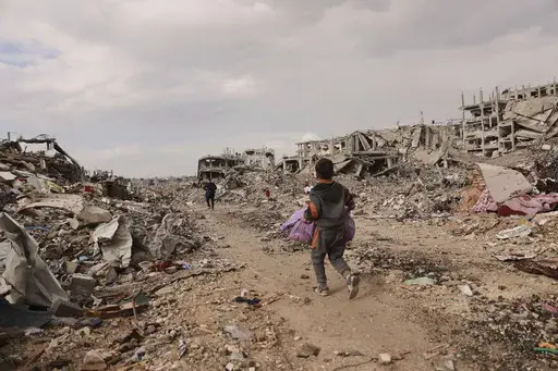 A Palestinian boy carries his belongings as he walks with his family next to the rubble of destroyed homes, after the ceasefire deal between Israel and Hamas, in Gaza City, Gaza Strip, Friday, Jan. 24, 2025. (AP Photo/Abed Hajjar)