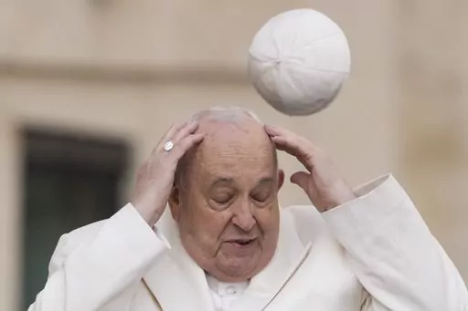 Pope Francis tries to catch his cap as wind blew it away while arriving for his weekly general audience in the St. Peter's Square at the Vatican, Wednesday, March 13, 2024. (AP Photo/Andrew Medichini, File)