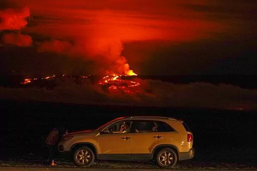 A man talks on a phone in his car alongside Saddle Road as the Mauna Loa volcano erupts Wednesday, Nov. 30, 2022, near Hilo, Hawaii. The world's largest volcano continues to erupt but scientists say lava is no longer feeding the flow front that has been creeping toward a crucial highway. That means the flow isn't advancing and is no longer an imminent threat to the road that connects the east and west sides of the Big Island. (AP Photo/Gregory Bull, File)