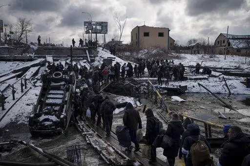 Ukrainians cross an improvised path under a destroyed bridge while fleeing Irpin, in the outskirts of Kyiv, Ukraine, Tuesday, March 8, 2022. As milestones go, the first anniversary of Russia's invasion of Ukraine is both grim and vexing. It marks a full year of killing, destruction, loss and pain felt even beyond the borders of Russia and Ukraine. (AP Photo/Felipe Dana, File)