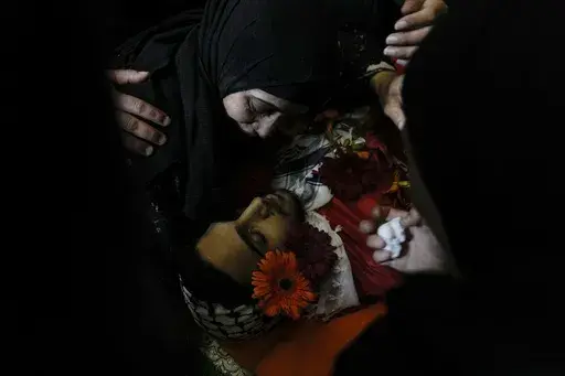 The mother of Ahmed Nidal Aslan, who was killed during clashes with Israeli forces, mourns over the body of her son during his funeral in the West Bank refugee camp of Qalandiya, Wednesday, July 24, 2024. The Palestinian health ministry said a man was shot dead Wednesday by Israeli fire in the central West Bank, as violence flares in the Israeli occupied territory. (AP Photo/Mahmoud illean)