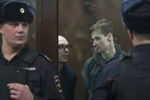 Artyom Kamardin, left, and Yegor Shtovba, right, stand behind a glass in a cage in a courtroom in Moscow, Russia, Thursday, Dec. 28, 2023. Artyom Kamardin was given a 7-year prison sentence Thursday for reciting verses against Russia's war in Ukraine, a tough punishment that comes during a relentless Kremlin crackdown on dissent. Yegor Shtovba, who participated in the event and recited Kamardin's verses, was sentenced to 5 1/2 years on the same charges. (AP Photo, File)