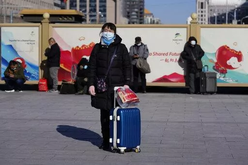 A traveler waits outside the Beijing railway station with her suitcase in Beijing, China, Friday, Jan. 28, 2022. The Beijing Winter Olympics is coinciding with the Chinese Lunar New Year and renewed Covid outbreaks prompting the Chinese authorities to call on the public to stay where they are instead of traveling to their hometowns for the year's most important family holiday. (AP Photo/Ng Han Guan)