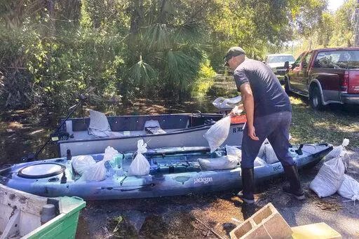 CORRECTS SPELLING OF LAST NAME TO MADLANG INSTEAD OF MADLING - Gabriel Madlang loads sandbags onto his kayak so he can fortify his house on a submerged street in Seminole County, Fla., on Sunday, Oct. 2, 2022. Residents in central Florida donned fishing waders, boots and bug spray and canoed or kayaked to their homes on streets where floodwaters continued rising Sunday despite it being four days since Hurricane Ian tore through the state. (AP Photo/Mike Schneider)