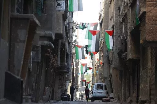 People walk under Palestinian flags in Yarmouk camp in Damascus Syria that has seen heavy fighting during the civil war, Wednesday, Nov. 2, 2022. A trickle of residents has returned to Yarmouk, the large Palestinian refugee camp-turned-Damascus neighborhood that was devastated in the country's civil war. (AP Photo/Omar Sanadiki, File)