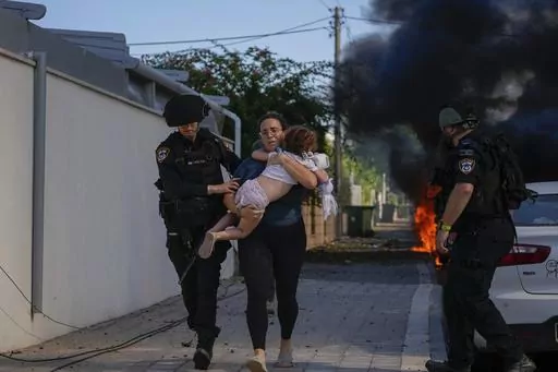 Israeli police officers evacuate a woman and a child from a site hit by a rocket fired from the Gaza Strip, in Ashkelon, southern Israel, Saturday, Oct. 7, 2023. Israel and Hamas have both been accused of breaking the rules of armed conflict. Hamas killed hundreds of civilians and abducted scores more when it attacked southern Israel on Oct. 7. Israel has bombarded Gaza and told more hundreds of thousands of Palestinians to leave their homes. The United Nations says it is collecting evidence of 