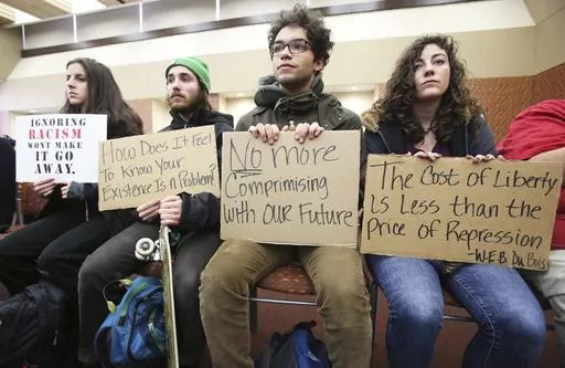 University of Wisconsin-Madison students, from left, Marisa Skelley, Martin Jarzyna, Sam Broadnax and Morgan Menke hold up signs protesting racism on campus during a meeting for the UW System Board of Regents on campus in Madison, Wis., Dec. 11, 2015. The debate over free speech and racial equity on Wisconsin's college campuses is intensifying. In a span of days after a student posted racial slurs, a top Republican proposed eliminating campus diversity offices and a medical college cancelled a d