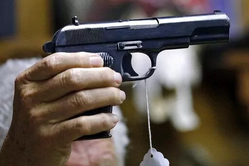 A sales clerk holds a pistol during an auction in Rochester, Wash., on Oct. 20, 2017. A study published in Annals of Internal Medicine on Monday, April 4, 2022, suggests people who live with handgun owners are murdered at more than twice the rate of people who live in homes without such firearms. (AP Photo/Elaine Thompson, File)