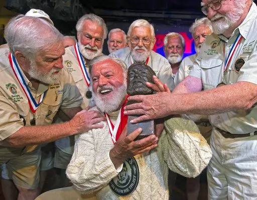 In this Saturday, July 23, 2022, photo provided by the Florida Keys News Bureau, Jon Auvil, center, receives an Ernest Hemingway bust and congratulations after he won the 2022 Hemingway Look-Alike Contest at Sloppy Joe's Bar in Key West, Fla. Left of Auvil is Joe Maxey, the 2019 winner, and at right is Fred Johnson, who won in 1986. Auvil, who finally won on his eighth attempt, beat 124 other entrants in the contest that was the highlight event of Key West's annual Hemingway Days festival that e