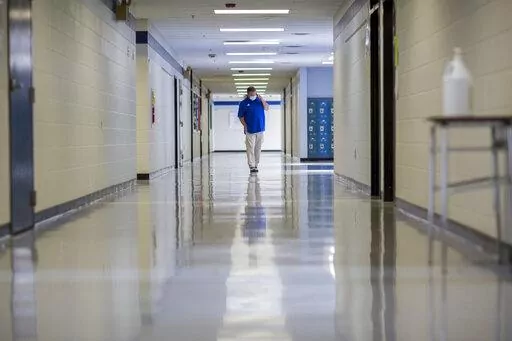 FILE - A middle school principal walks the empty halls of his school as he speaks with one of his teachers to get an update on her COVID-19 symptoms, Friday, Aug., 20, 2021, in Wrightsville, Ga. On Monday, Dec. 27, 2021, U.S. health officials cut isolation restrictions for Americans who catch the coronavirus from 10 to five days, and also shortened the time that close contacts need to quarantine. (AP Photo/Stephen B. Morton, File)