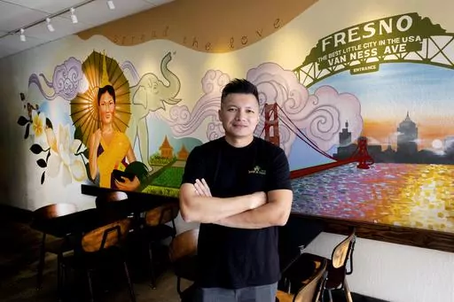 David Rasavong stands by a mural depicting his family's journey from Laos to San Francisco and then to Fresno, in his restaurant "Love & Thai" in Fresno, Calif. on Wednesday, Dec. 20, 2023. Rasavong's body still tenses up when recounting how a so-called animal welfare crusader in May implied on social media that his 7-month-old restaurant, Tasty Thai, owned a pitbull tied up at a home next door. What's more, the dog would eventually be meal fodder. By the next day, vitriolic comments, voicemails